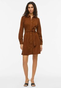 Robe en velours côtelé marron avec manches longues, boutonnée sur le devant et détail de taille nouée. Comprend un col et un ourlet arrivant au genou. Sandales noires style mule.