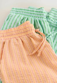 Twee paar gestreepte shorts met elastische taillebanden en koorden, de ene oranje met roze strepen, de andere lichtblauw met groene strepen.