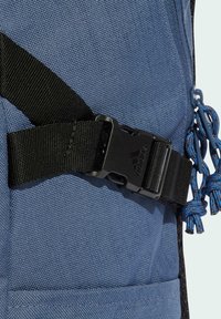 Blue fabric backpack section with black nylon strap, plastic buckle, and blue drawstring accents. Textured surface with reinforced stitching.