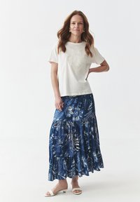 Cămașă albă cu mânecă scurtă, cu detalii brodate în formă de frunză, asortată cu o fustă maxi tiered cu model floral albastru. Purtați cu sandale albe.