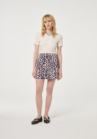 Korte mouwen crème top gecombineerd met een roze minirok met luipaardprint. Het model draagt zwarte platte schoenen met decoratieve accenten. Eenvoudig en modern ontwerp.