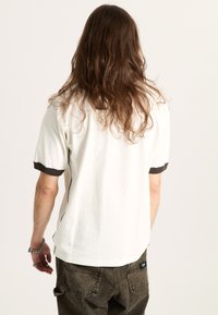 Camiseta de algodón blanca de manga corta con puños de canalé marrón oscuro, corte relajado y costuras decorativas a lo largo de las costuras laterales.