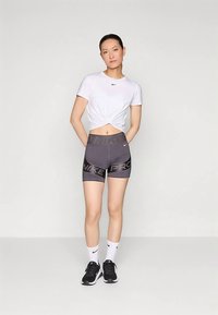 Valge lühendatud t-särk esipainutusega, hallid Nike Pro lühikesed püksid logoga, mustad tennised ja valged sokid mustade detailidega.