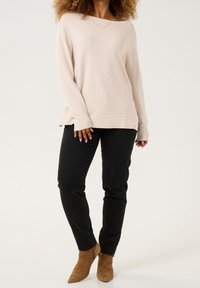 Maglione a costine beige chiaro con scollatura ampia, abbinato a pantaloni neri aderenti e stivaletti in suede beige.