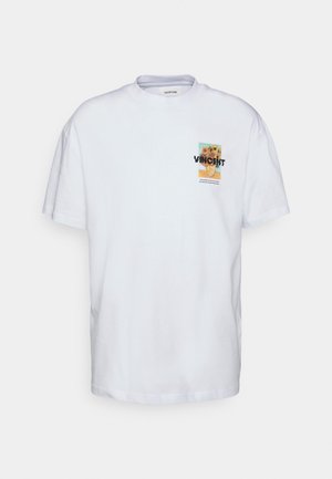 Persoon die een blauwe en witte geruite jas draagt, een wit T-shirt met afbeelding, beige broek en zwart-witte geruite instapschoenen.