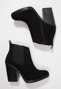 Bottines en daim noir avec un talon épais, fermeture éclair latérale et panneaux élastiques pour un ajustement parfait. Texture lisse avec un design à bout arrondi.