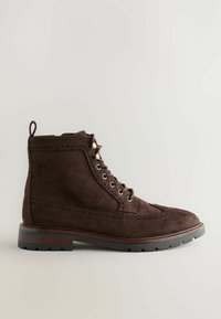 Bruine suède enkellaars met decoratieve perforaties, geveterd met metalen oogjes en een stevige rubberen zool.