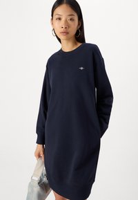 Abito felpa blu navy con maniche lunghe, collo a giro e tasche laterali; presenta un piccolo logo ricamato sul petto.
