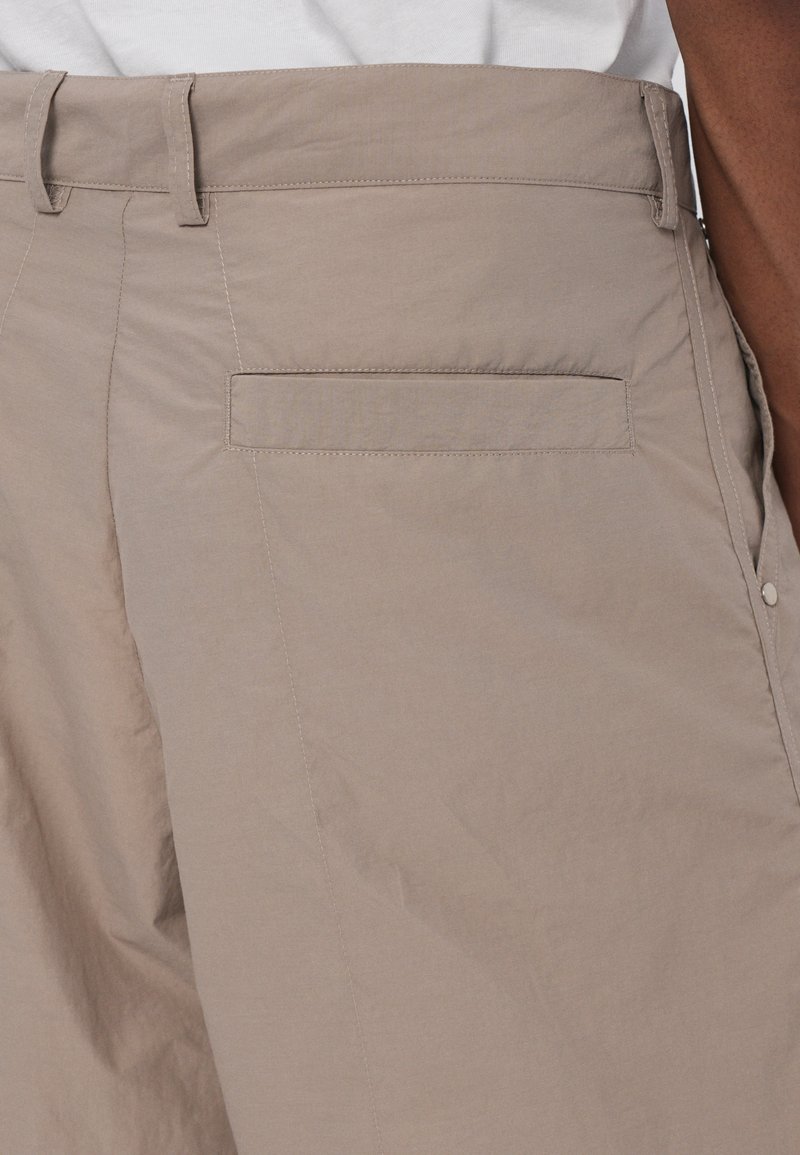 Beige cotton-blend trousers with a smooth texture, featuring a single back pocket and matching stitching along the side seams.