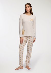 Set di pigiama beige chiaro composto da una maglia a maniche lunghe con una grafica di un orso e la scritta 'LOVE', abbinata a pantaloni decorati con facce di orso.