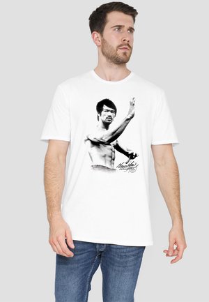 Weißes Baumwoll-T-Shirt mit einem Schwarz-Weiß-Grafik eines oberkörperfreien Mannes in einer Kampfsportpose, mit einer gedruckten Unterschrift darunter.