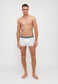 Białe bawełniane bokserki z czarnym elastycznym pasem z logo "justcavalli". Model stoi boso, patrząc na wprost.