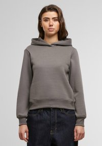 Haut en coton gris avec une poche avant et une capuche doublée, présenté avec un jean en denim foncé, doté de poignets et d'une taille côtelés.