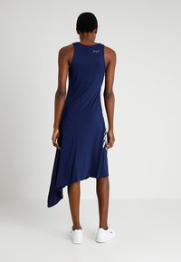 Granatowa sukienka bez rękawów z zaokrąglonym dołem, wykonana z miękkiego materiału. Posiada detal z logo na plecach i stylizowana jest z białymi sneakersami.