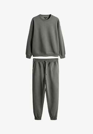 Pelēka kokvilnas maisījuma džemperis ar apaļu apkakli un garām piedurknēm, kopā ar pelēkām džogera biksēm ar elastīgu jostasvietu un sānu kabatām.