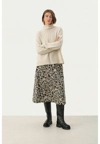 Pull en col roulé beige, ourlet côtelé, associé à une jupe midi imprimée léopard et des bottes noires montantes à semelle épaisse.