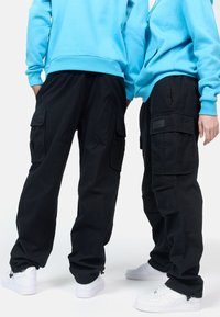 Black cargo pants with side pockets, paired with bright blue hoodies. White sneakers with a textured sole. Simple, relaxed fit design.