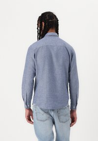 Maglietta blu a maniche lunghe in tessuto texture, con colletto classico e polsini con bottoni, abbinata a jeans di denim azzurri.