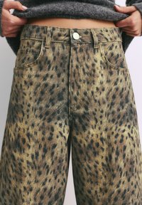 Jeans z leopardjim vzorcem iz denima z visokim pasom, globokimi žepi in teksturirano tkanino v mešanici bež in črnih pik.