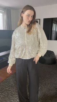 Hopeinen paljetti-bomber-takki, jossa resorit hihansuissa ja helmassa, yhdistettynä mustiin housuihin. Pinta kimaltelee heijastavilla tekstuureilla.