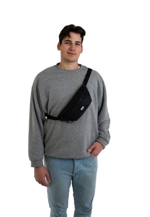 Marsupio in tessuto nero con una tasca con zip, indossato a spalla. Il modello indossa un maglione grigio a girocollo e jeans azzurri chiari.