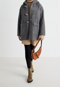 Grå uldduffelcoat med træknapper, to forlommer, kombineret med en beige sweaterkjole, sorte strømpebukser, grønne ankelstøvler og en brun håndtaske.