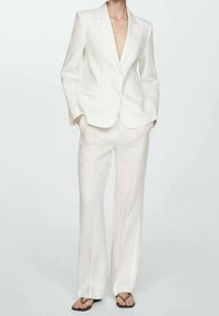 Witte linnen pak bestaande uit een op maat gemaakte blazer met twee knopen en een broek met brede pijpen. Het materiaal heeft een gestructureerde afwerking.