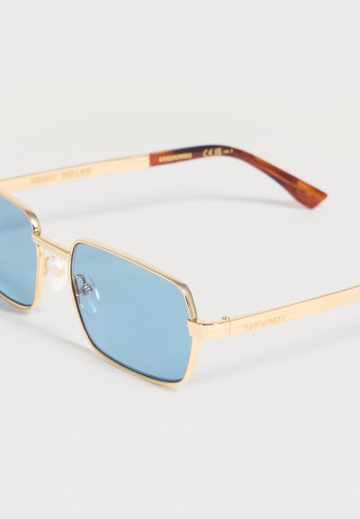 Γυαλιά ηλίου με χρυσό μεταλλικό σκελετό, μπλε ορθογώνιους φακούς και άκρες βραχίονα με σχέδιο καβούρας σε ανοιχτό φόντο.