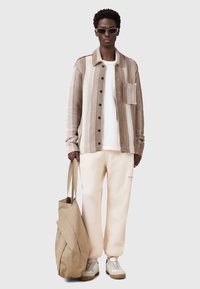 Gestreepte beige en bruine shirtjack, wit t-shirt, lichtroze joggingbroek, beige stoffen schoudertas en lichte sneakers met textuurzolen.