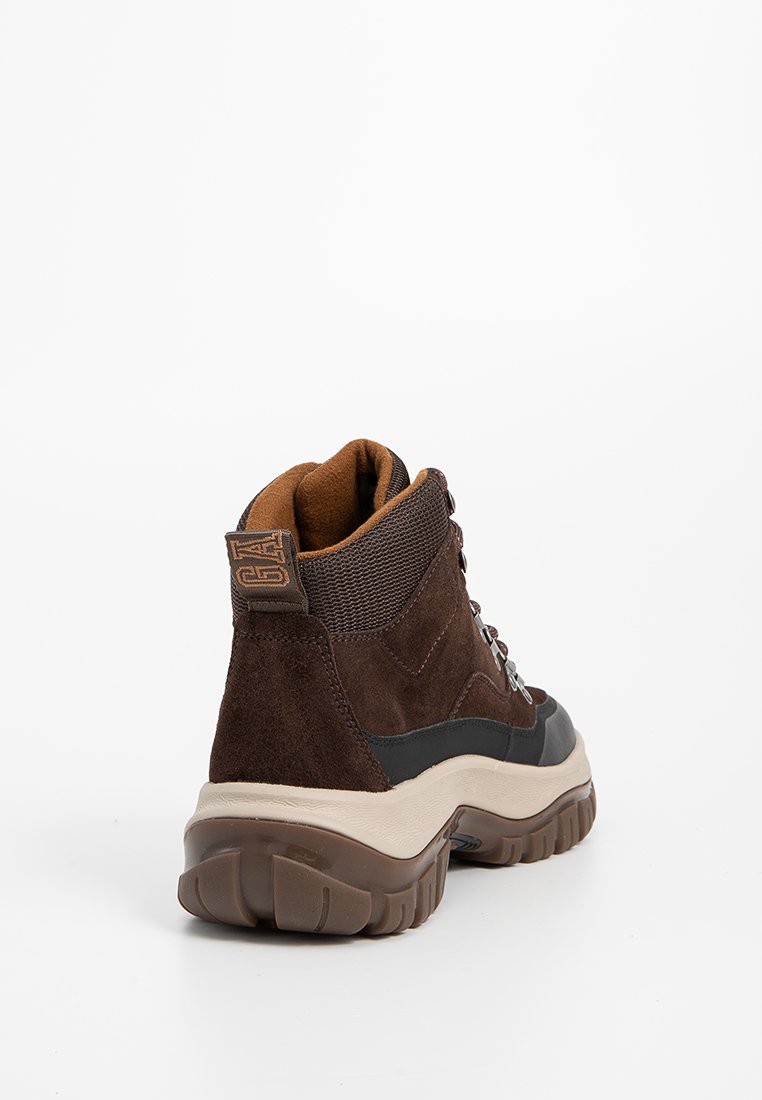 Bruine suède wandelschoenen met een stevige beige rubberen zool, een textiele kraag en metalen oogjes voor de veters. Het achterlabel heeft het logo.