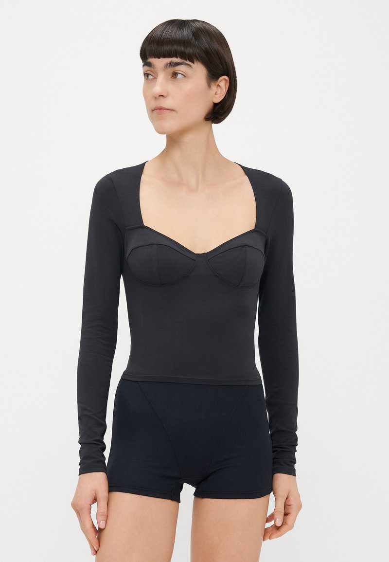 Body noir à manches longues avec un décolleté carré, doté de bonnets rembourrés et d'une coupe ajustée, accompagné de shorts noirs taille haute.