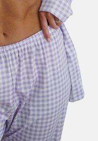 Purple checkered pajama set made of soft fabric, featuring elastic waistband and loose fit, with a shirt having long sleeves and a relaxed cut.