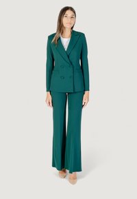 Blazer teal doppiopetto con rever e pantaloni a zampa abbinati, realizzati in tessuto liscio, abbinati a una maglietta bianca e tacchi beige.