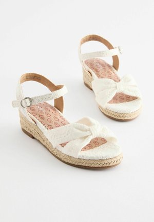 Vita klacksandaler med en vävd jute sula, tygrosett och justerbar ankelrem. Den vadderade innersulan har ett blommigt mönster.