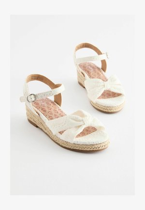Fehér, wedges szandál, szőtt juta talppal, textil masnival és állítható bokapánttal. A párnázott talpbetét virágmintás.