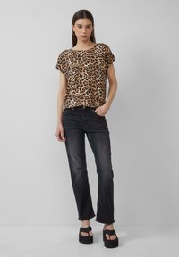 Blouse à manches courtes en imprimé léopard beige et noir, associée à un jean noir. Le modèle porte des sandales à plateforme noires et épaisses. Fond uni clair.