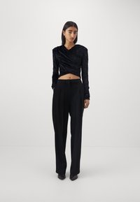 Musthave musta pikkade varrukatega top, millel on tekstureeritud kangas ja vöödisain, koos kõrge vöökoha ja laia säärega mustade pükstega ning teravate mustade kingadega.