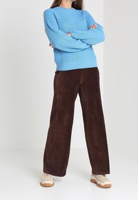 Vaaleansininen paksu neulepaita yhdistettynä ruskeisiin leveälahkeisiin corduroyhousuihin ja beigen värisiin lenkkareihin. Yksinkertainen muotoilu, teksturoitu kangas, rento istuvuus.