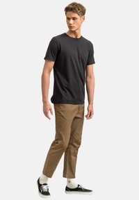 Zwarte katoenen T-shirt met korte mouwen, gecombineerd met beige chino's en zwarte sneakers. Aangevuld met gestreepte witte sokken.