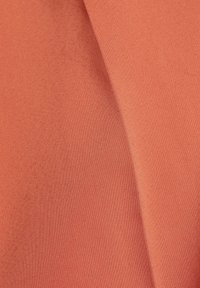 Tissu tissé lisse de couleur corail douce unie, avec un pli délicat créant une ombre douce sur la surface.