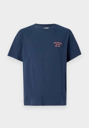Camiseta de algodón azul marino con cuello redondo, mangas cortas y un pequeño gráfico rojo en el lado izquierdo del pecho que dice "POR EL VIAJE DE LA VIDA EST. 1947."