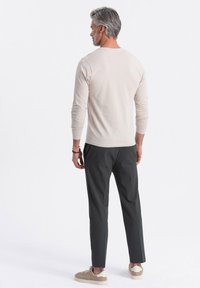 Helles beige Langarmhemd, kombiniert mit dunklen Hosen. Das Hemd hat einen runden Halsausschnitt und eng anliegende Ärmel. Die Schuhe sind hell gefärbt.