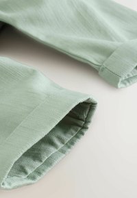 Tessuto verde chiaro con un motivo a spina di pesce testurizzato, con polsini arrotolati e una finitura liscia.