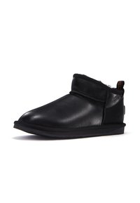 Botas de tobillo de cuero negro con punta redonda, forro interior suave y suela plana de goma. Presentan una costura y una pequeña lengüeta en el talón.