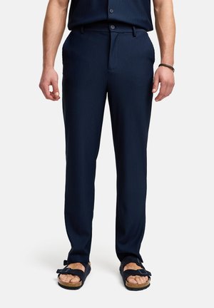 Marinrandiga byxor i lättviktsmaterial, med flat front, bältesöglor och skräddarsydd passform, tillsammans med mörka sandaler.