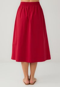 Jupe A-line rouge en coton, dotée d'une taille élastique. Le design arrive au genou, avec une finition lisse et un ourlet simple sans embellissements.