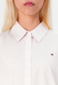 Camicia collare a righe rosa chiaro realizzata in cotone, caratterizzata da un piccolo logo ricamato sul petto e una chiusura con bottoni.
