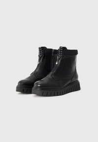 Bottines en cuir noir avec fermeture éclair, accents côtelés en haut et semelle épaisse à motifs pour traction et durabilité.