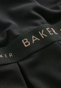 Černá tkanina se hladkým povrchem, která má zelený pás s výšivkou "BAKER" v kovově zlaté barvě.