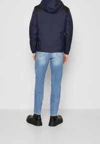Giacca a vento navy con dettagli neri sulle spalle, abbinata a jeans skinny azzurri e stivali neri chunky. Tessuto morbido, design aderente.